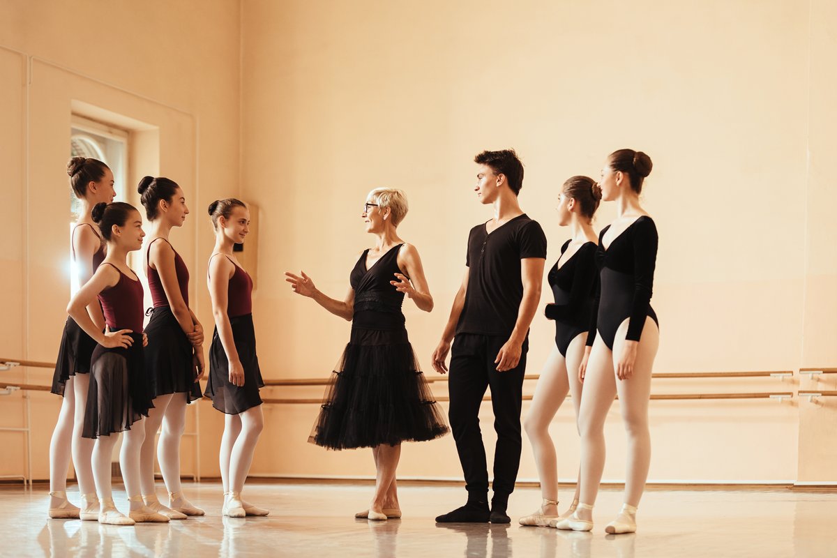 Ballet teacher giving notes to a group of dancers in a studio