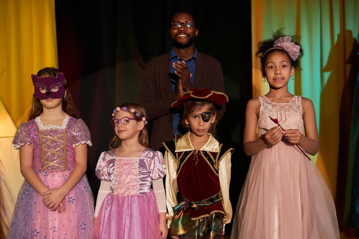 Children in costume on stage with their director during a summer show