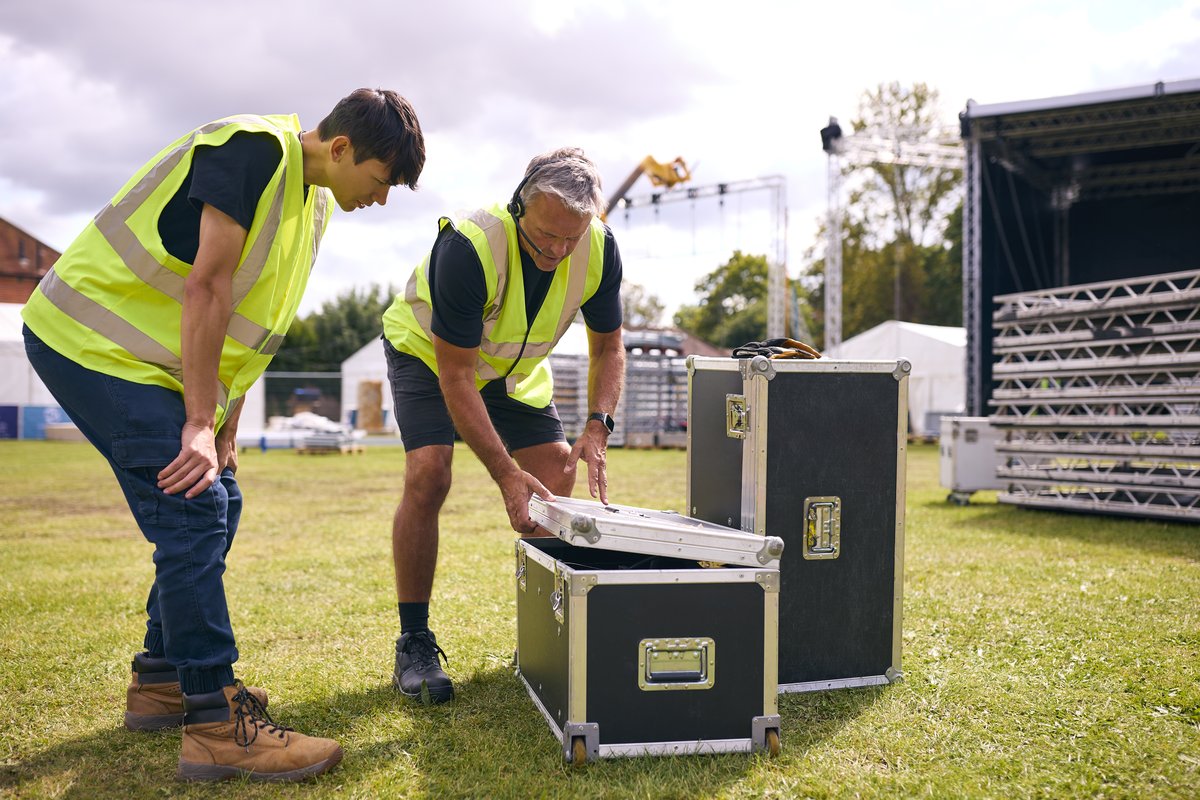 Crew members unpacking road cases beside an outdoor stage Crew members unpacking road cases beside an outdoor stage